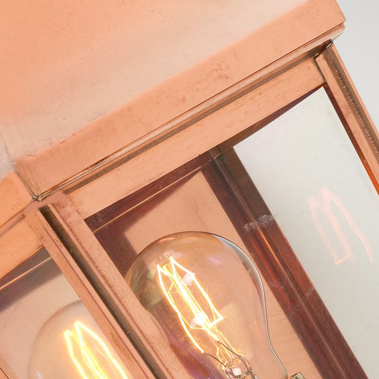 Close-up of the Chelsea Outdoor 1 Light Small Half Lantern in copper, featuring a light bulb that emits a warm glow. The glow is visible through the reflective glass panels, and the lantern's slightly weathered metal frame gives it a rustic look. This IP44 rated copper fixture ensures reliable lighting in any weather condition.