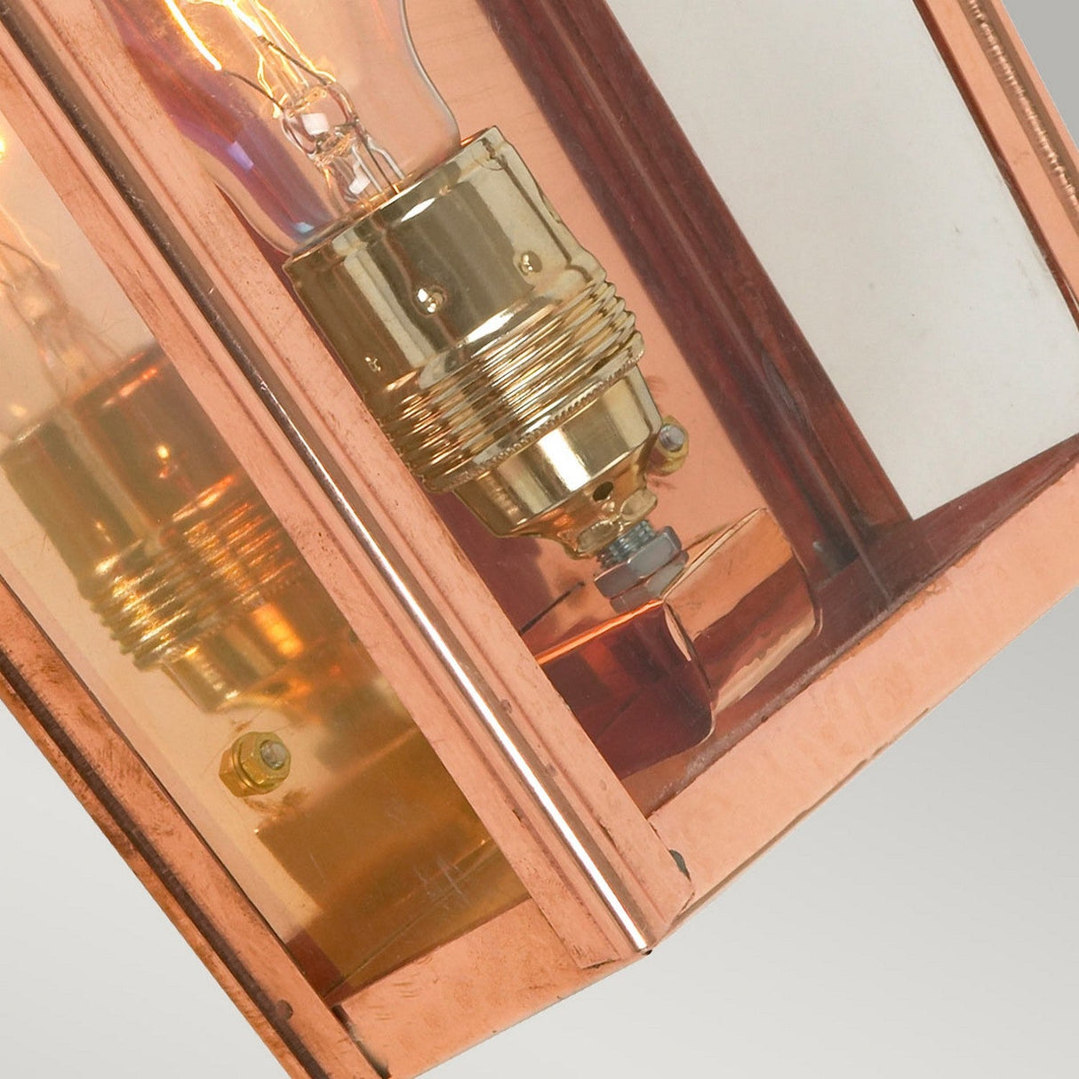 A close-up of the Chelsea Outdoor 1 Light Small Half Lantern in copper reveals a brass light bulb socket. The partially visible bulb and the angled positioning of the half lantern reflect light off its metallic surfaces, showcasing the allure of IP44 rated lighting.