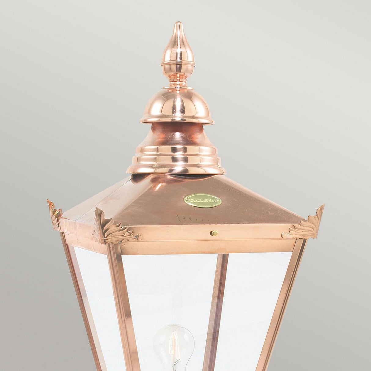 The Chelsea 1 Light Grande Lamp Post Head - Copper is a striking lantern with a pyramid-shaped top and finial, featuring glass panels and a visible bulb, making it perfect for enhancing your outdoor lighting against any plain background.