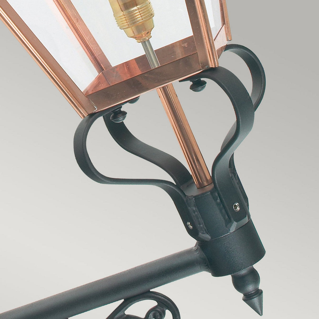Close-up of the Chelsea Outdoor 1 Light Grande Up Wall Lantern in copper, showcasing a blend of black metal and copper design. It is mounted on a metal bracket featuring elegant scrollwork details. With an IP44 rating, this lantern is ideal for outdoor use.