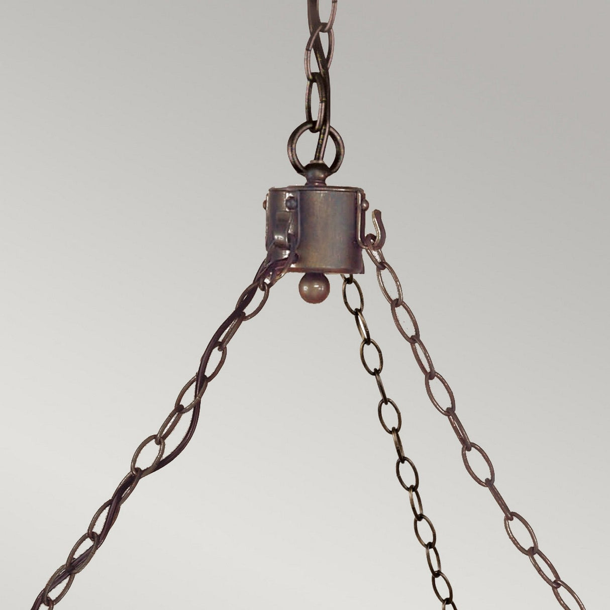 The Cromwell 12 Light Chandelier in Old Bronze features a design with three metal chains that converge at a central point and are attached to a circular metal component. This fixture brings out a vintage or industrial style accented with medieval charm, perfectly set against a plain, light gray background.