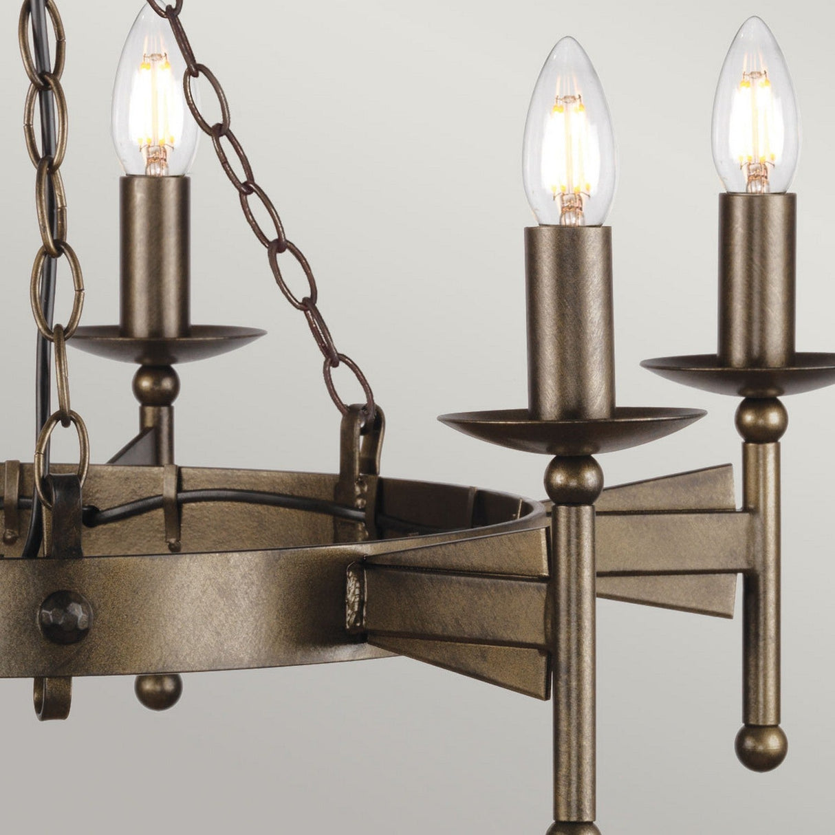 Capture a close-up of the Cromwell 6 Light Chandelier - Old Bronze, featuring three illuminated candle-style bulbs. This chandelier is crafted from solid iron with dark bronze chains and a geometric frame, all showcased against a soft beige background.