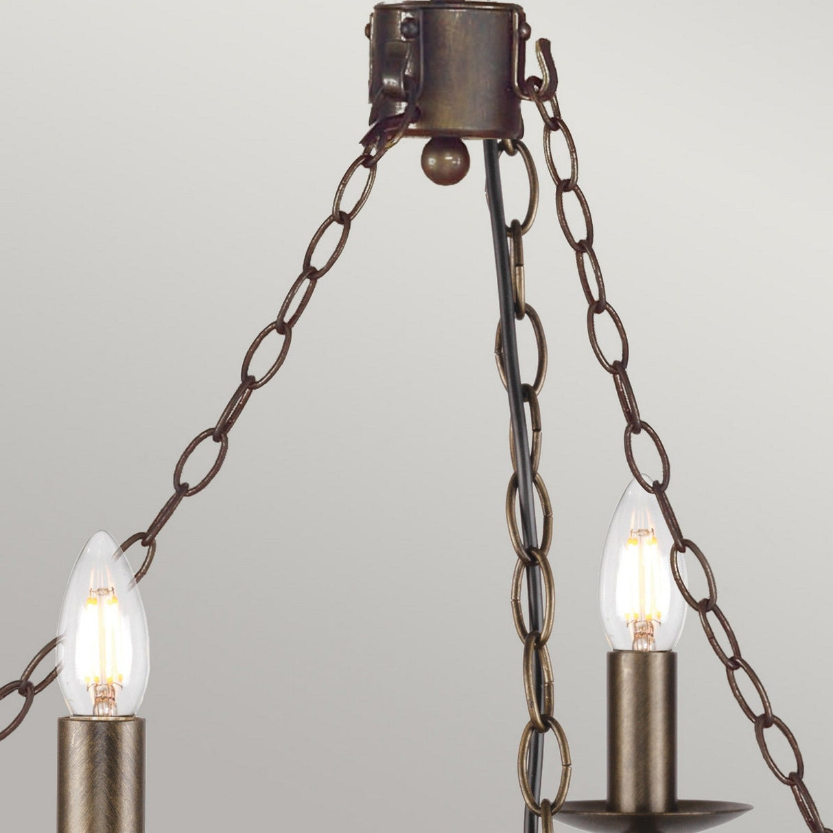 Close-up of the Cromwell 6 Light Chandelier in Old Bronze, showcasing its vintage-style design with two candle-shaped light bulbs suspended by three bronze chains. It stands elegantly against a plain light gray background.