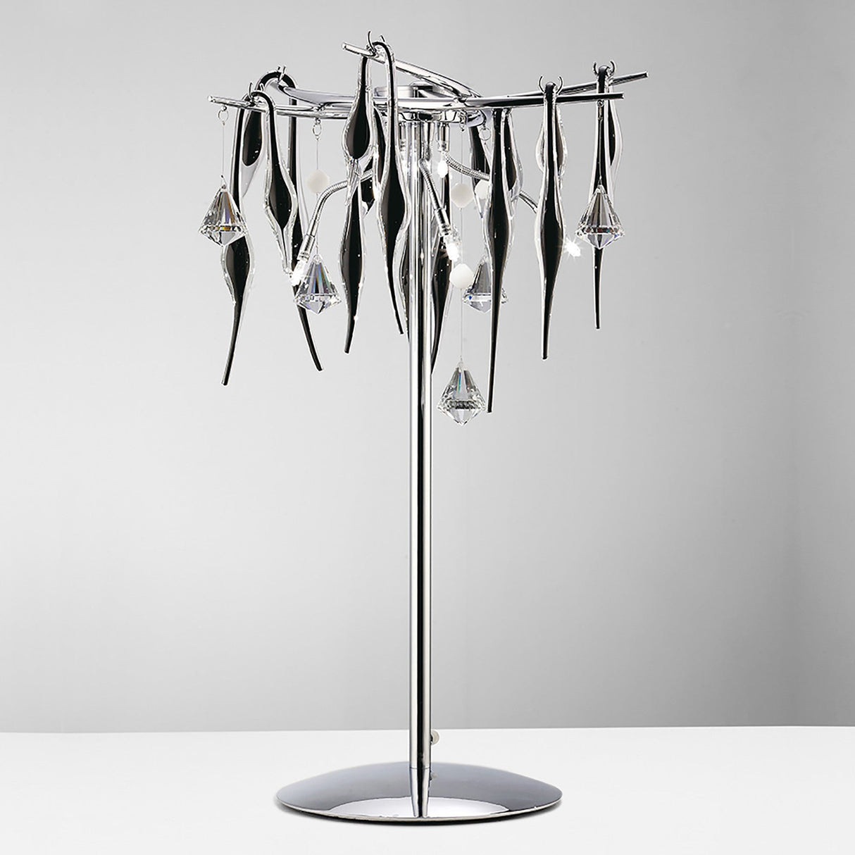 The Cygnet 6 Light Crystal Table Lamp features a sleek chrome base with black glass and dangling crystal-like pendants, adding a touch of luxury to any plain light background.