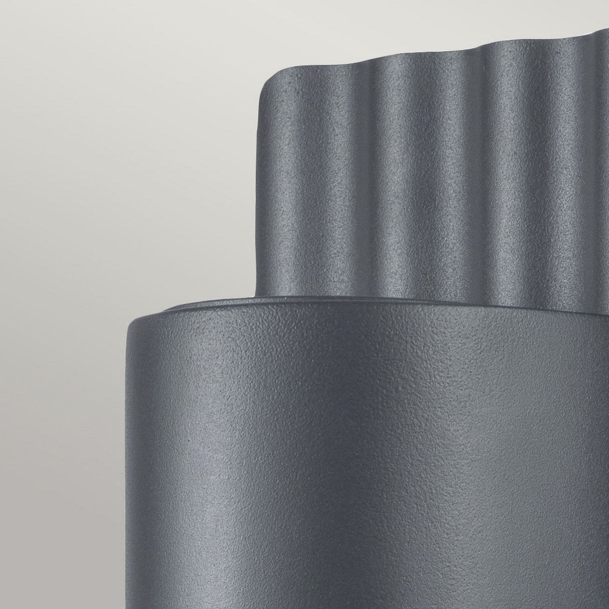 Close-up of the Dali Outdoor Wall Light - Grey, a textured gray cylindrical object featuring a wavy top edge against a plain light background. Its surface has a matte and slightly rough finish, showcasing its modern design and durable stainless steel construction.