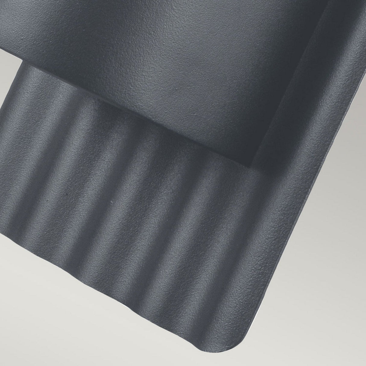 A close-up of the Dali Outdoor Wall Light in Grey reveals a textured, dark gray metal surface with a ridged, wavy pattern along its bottom edge. The durable stainless steel maintains a matte and robust appearance, casting subtle shadows that emphasize its corrugated design against a light background—embodying true minimalism in style.
