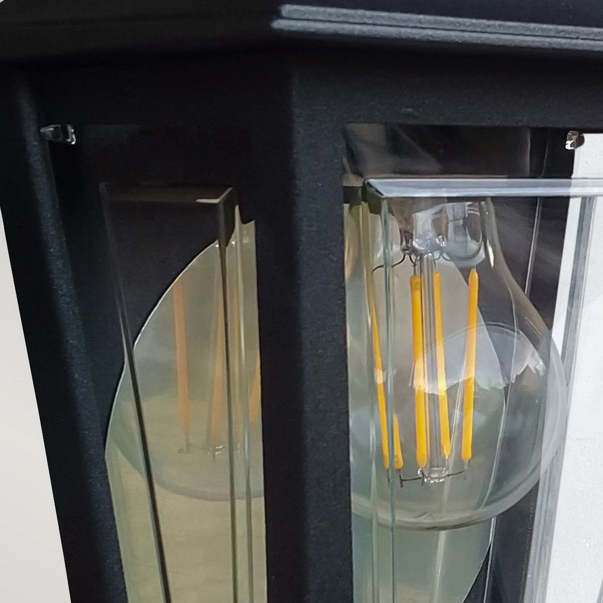 Close-up of a transparent light bulb inside the Deco Outdoor Wall Lantern - Black. The bulb's visible yellow filaments glow against a reflective surface, showcasing both style and resilience in this outdoor wall light.