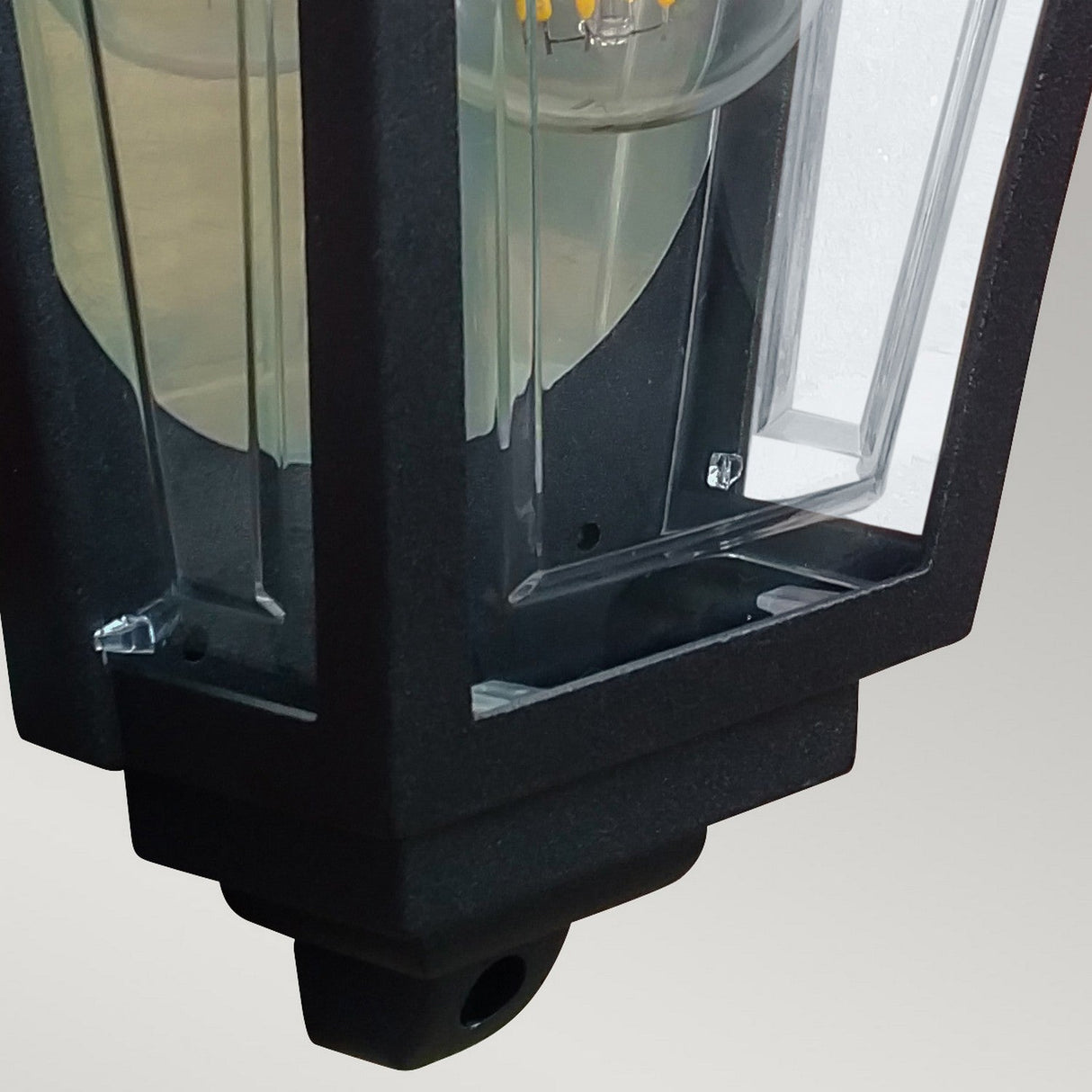 Close-up of the Deco Outdoor Wall Lantern - Black, featuring a clear glass enclosure that reveals an LED bulb inside. This lantern showcases a classic design with a rectangular frame and smooth surface, offering durable charm suitable for garden or patio lighting.