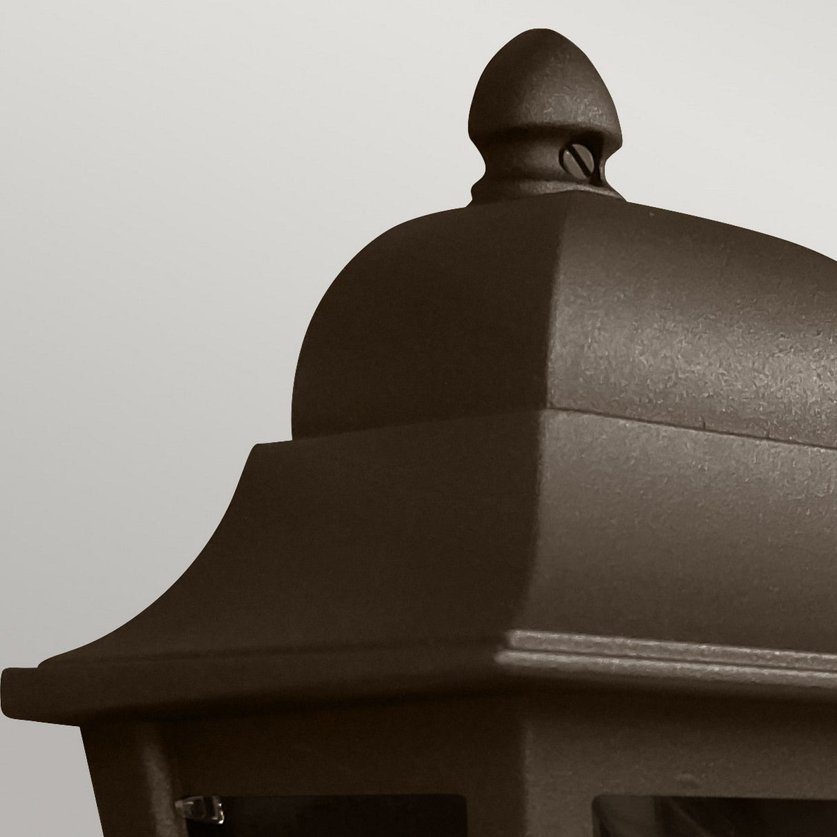 Close-up of the Deco Outdoor Wall Lantern - Bronze, featuring a textured metal surface. This lantern showcases a traditional half-lantern design with a detailed finial on top and a geometric pattern, set against a plain gray background.