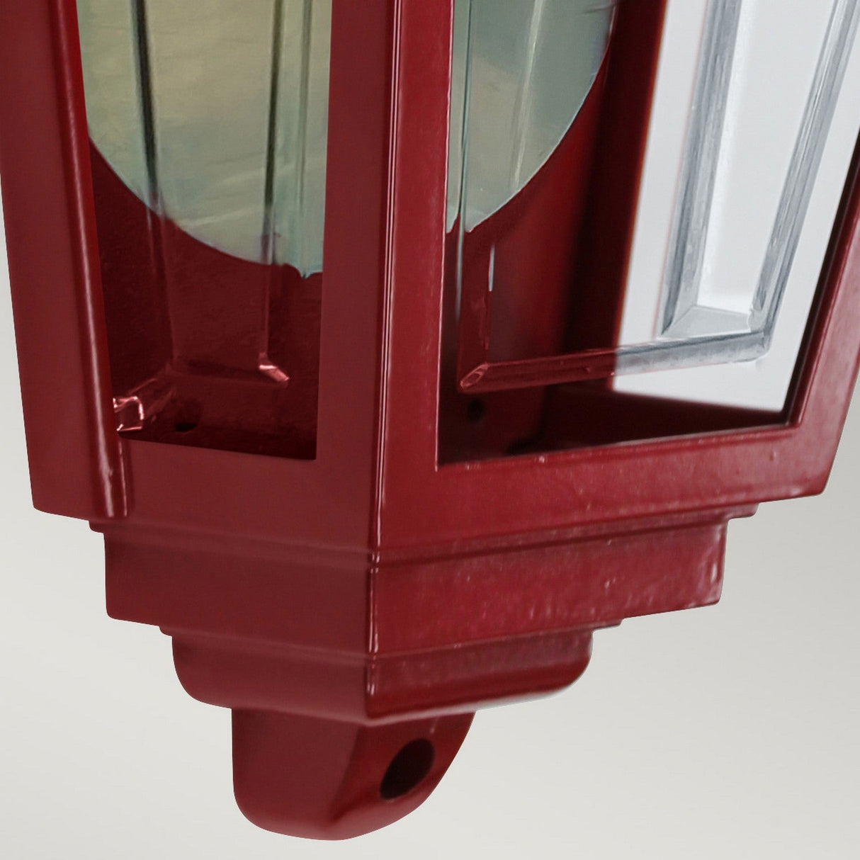Close-up of the Deco Outdoor Wall Lantern - Red, featuring decorative red metalwork and glass panels, highlighting its detailed craftsmanship and mirrored backplate against a light gray background.