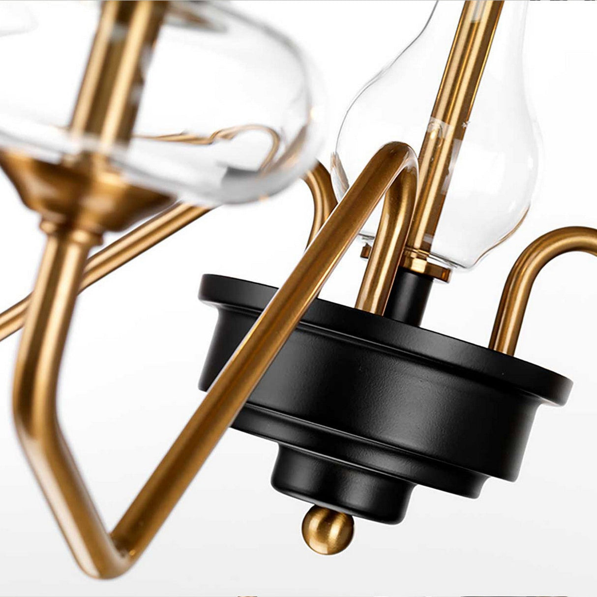 An up-close look at the Armand 3 Light Chandelier highlights its contemporary style with a blend of aged brass plated and charcoal black painted metal. This design showcases beautifully curved arms and elegant glass shades, crafting a sophisticated and modern lighting aesthetic.