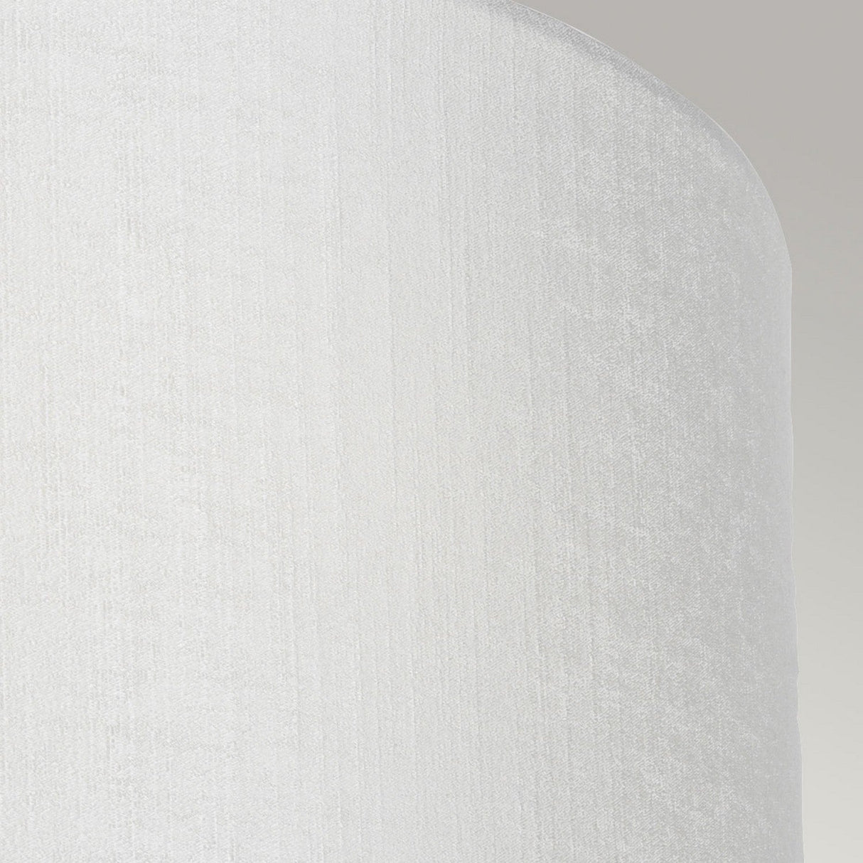 A close-up of the Cooper Large Curved Wall Light – Aged Brass reveals its vintage charm and textured cylindrical shade set against a light gray background. The visible curved side showcases a fabric pattern reminiscent of an aged brass finish.