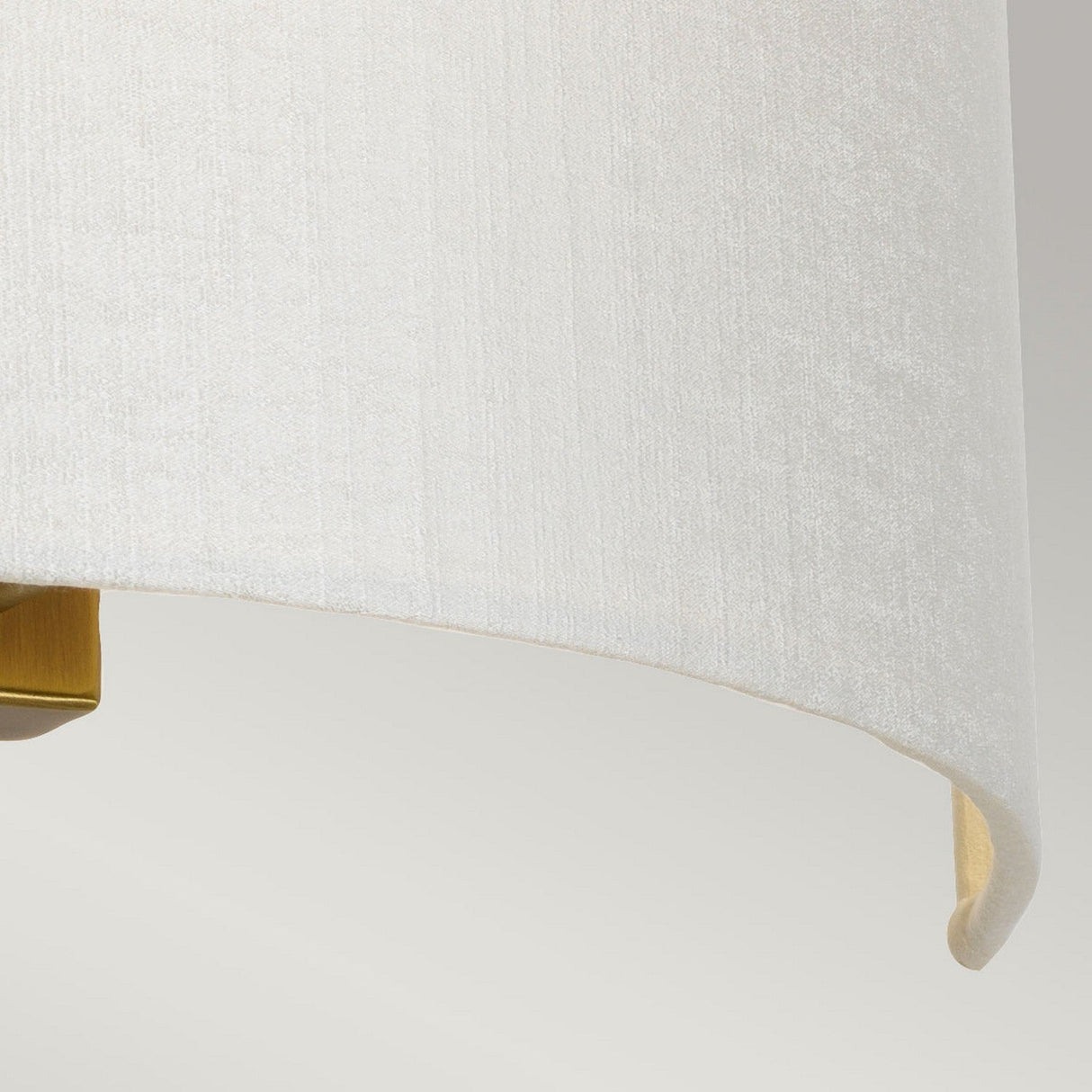 Close-up of the fabric lampshade from the Cooper Large Curved Wall Light in Aged Brass, showcasing its light color, smooth texture, and rounded edges that exude vintage charm. A small portion of the aged brass fixture peeks out beneath the shade, set against a softly blurred background.