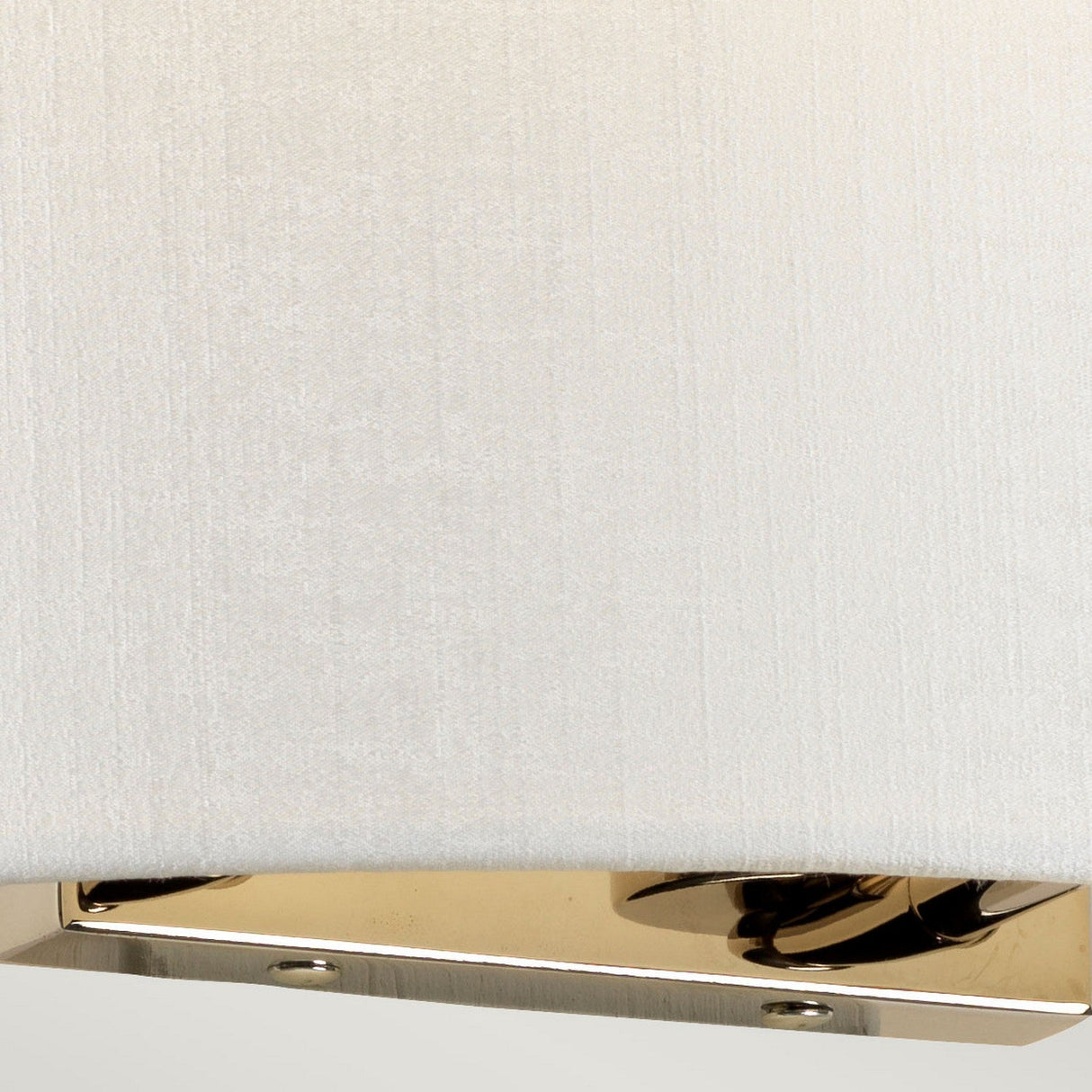 A close-up image of the Cooper Large Curved Wall Light showcases a faux silk shade paired with a polished chrome base accented with screws. The chrome surface elegantly reflects ambient lighting and surrounding elements.