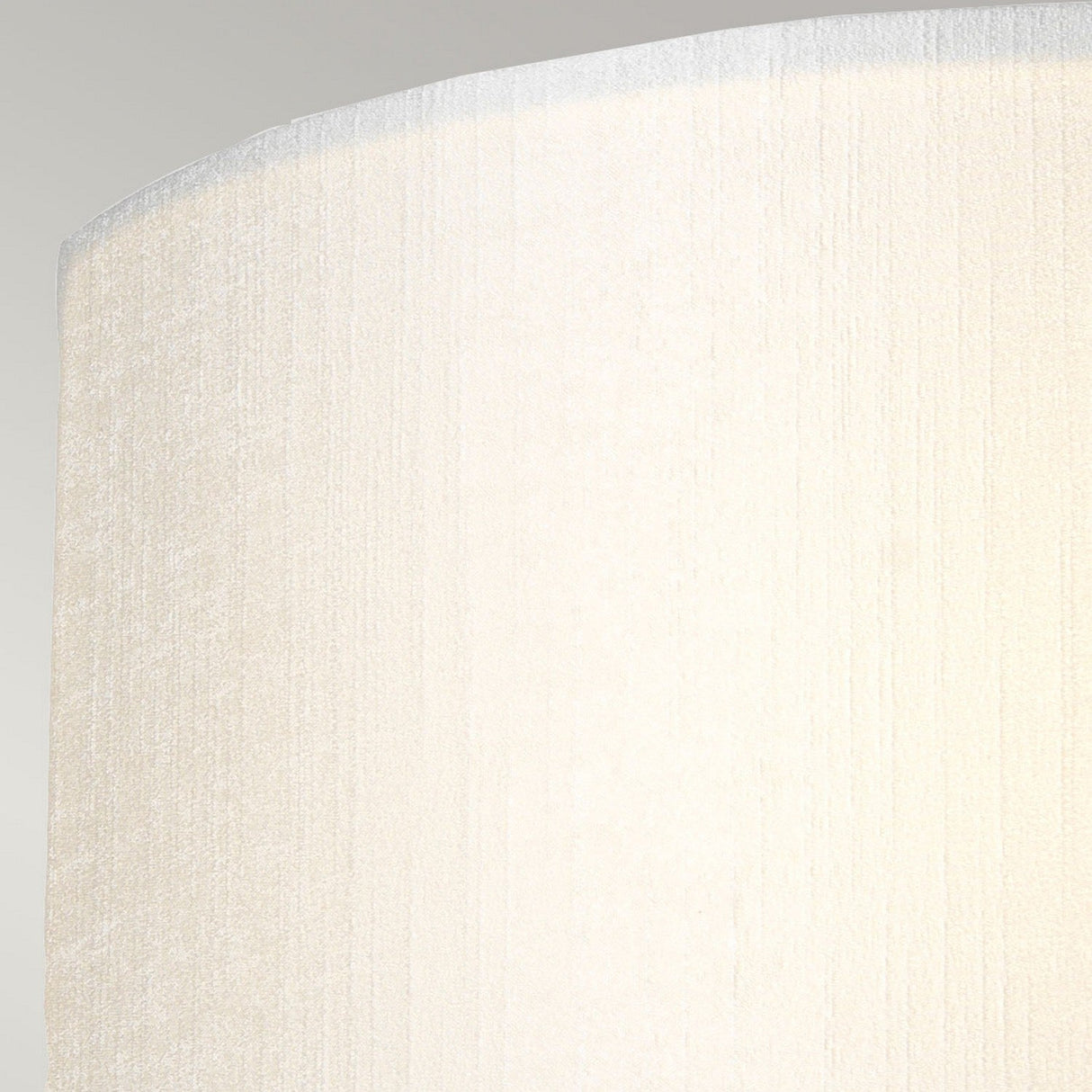 Close-up of the top section of a beige cylindrical lampshade with a textured fabric surface, softly illuminated from within, set against a neutral background. This faux silk shade pairs elegantly with the Cooper Medium Curved Wall Light in aged brass for a timeless look.
