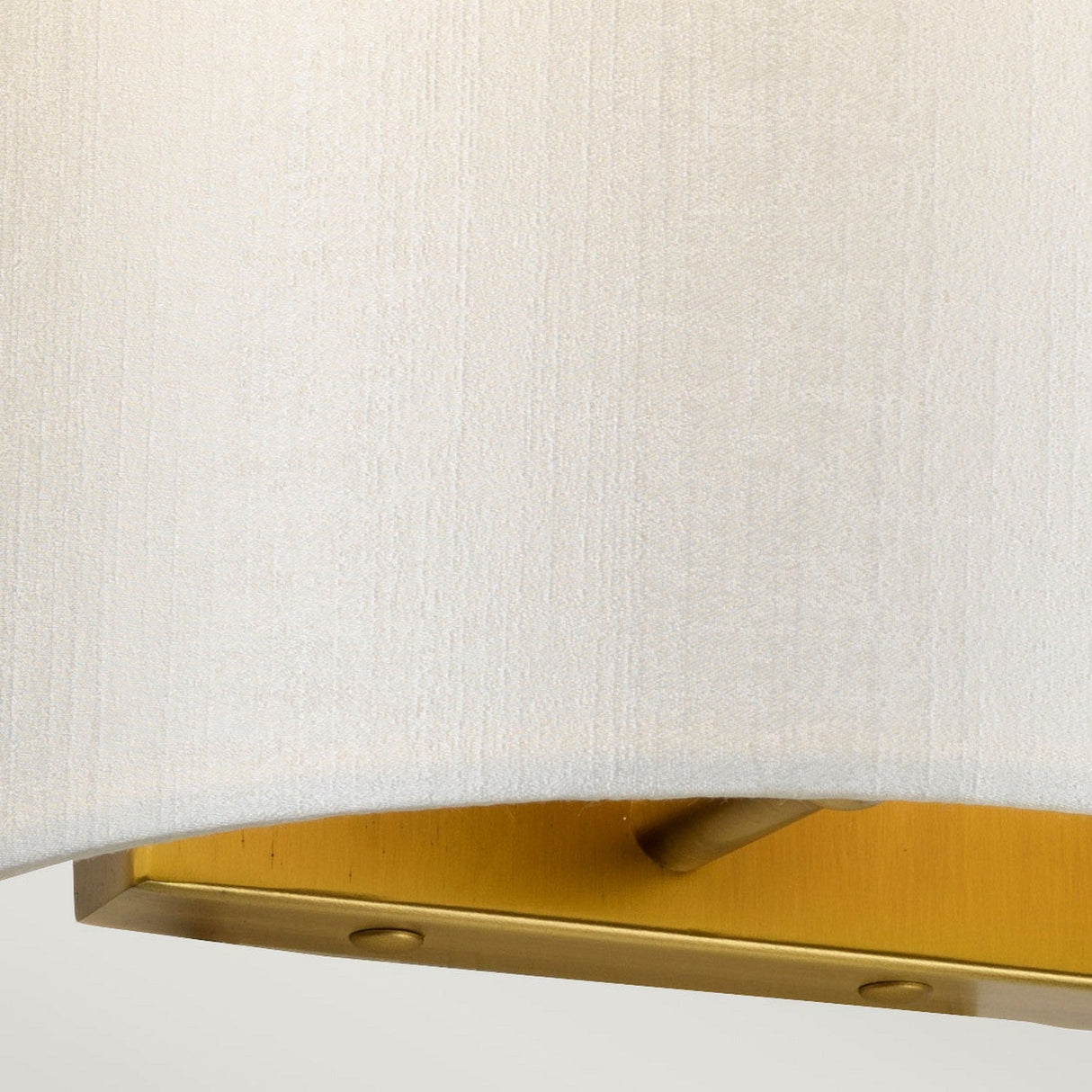 Close-up of the Cooper Small Curved Wall Light in aged brass, featuring a beige fabric lampshade. The textured surface of the lampshade accentuates the seamless blend between fabric and metallic elements, ideal for enhancing ambient lighting in any space.