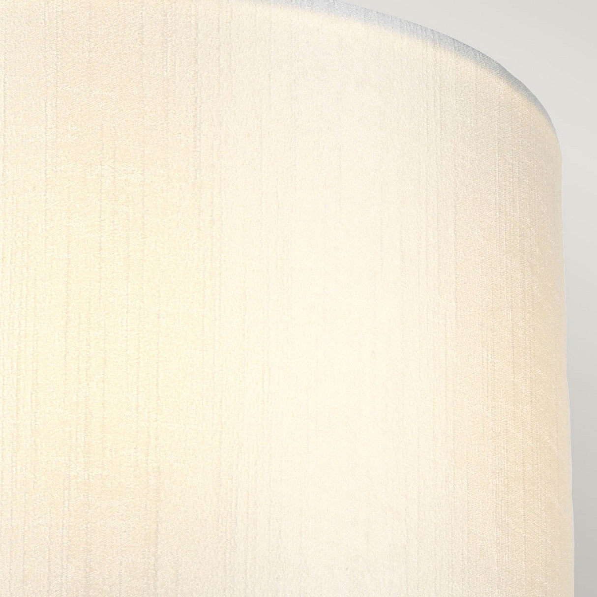 Close-up of a textured, cream-colored cylindrical surface, part of the Cooper Small Curved Wall Light - Aged Brass. The ambient lighting highlights subtle vertical patterns on the fabric, creating a soft and neutral appearance.