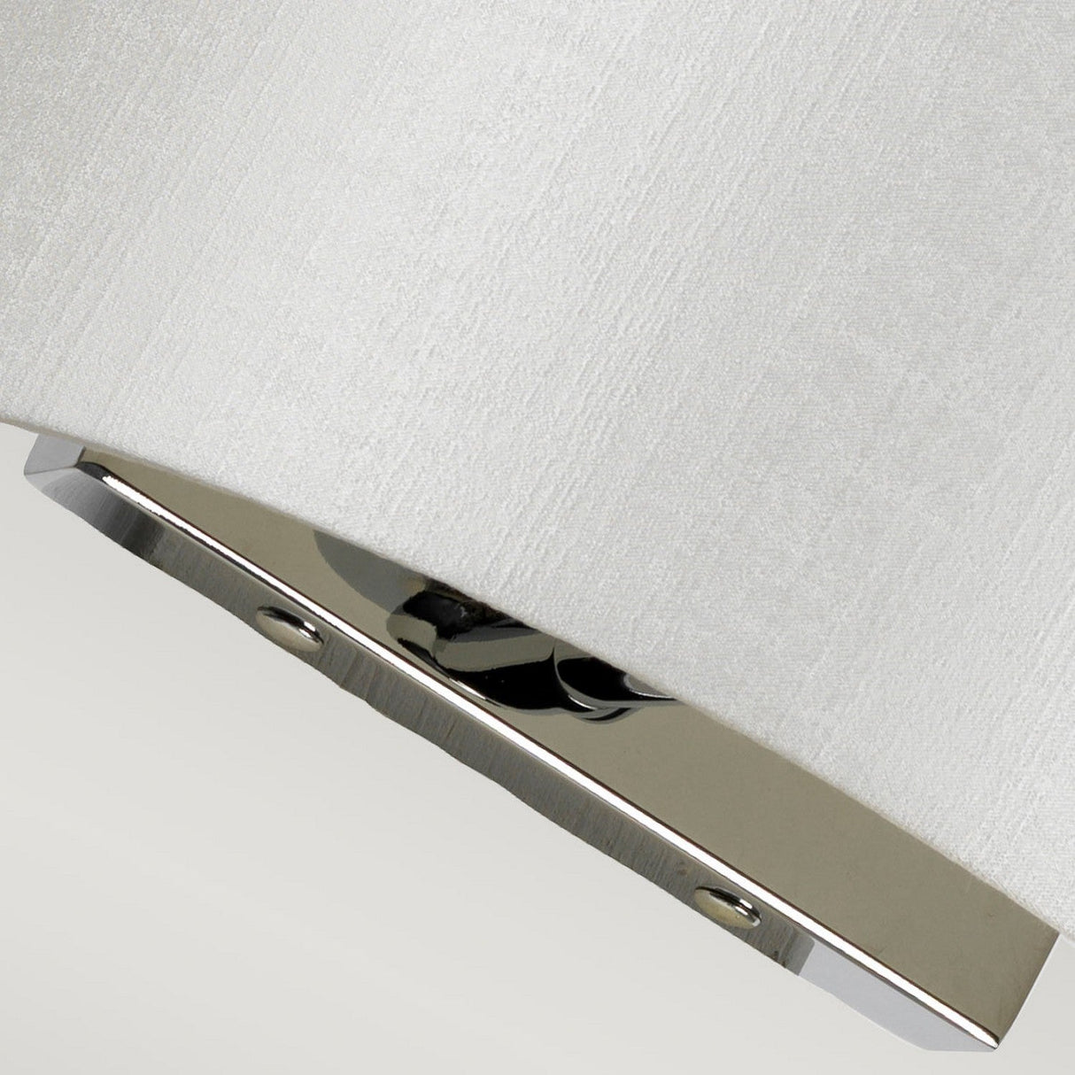 Close-up of the Cooper Small Curved Wall Light - Polished Chrome, featuring a sleek design with a light-colored fabric shade and a polished chrome base. This compact wall fixture is elegantly secured with two screws against a plain background.