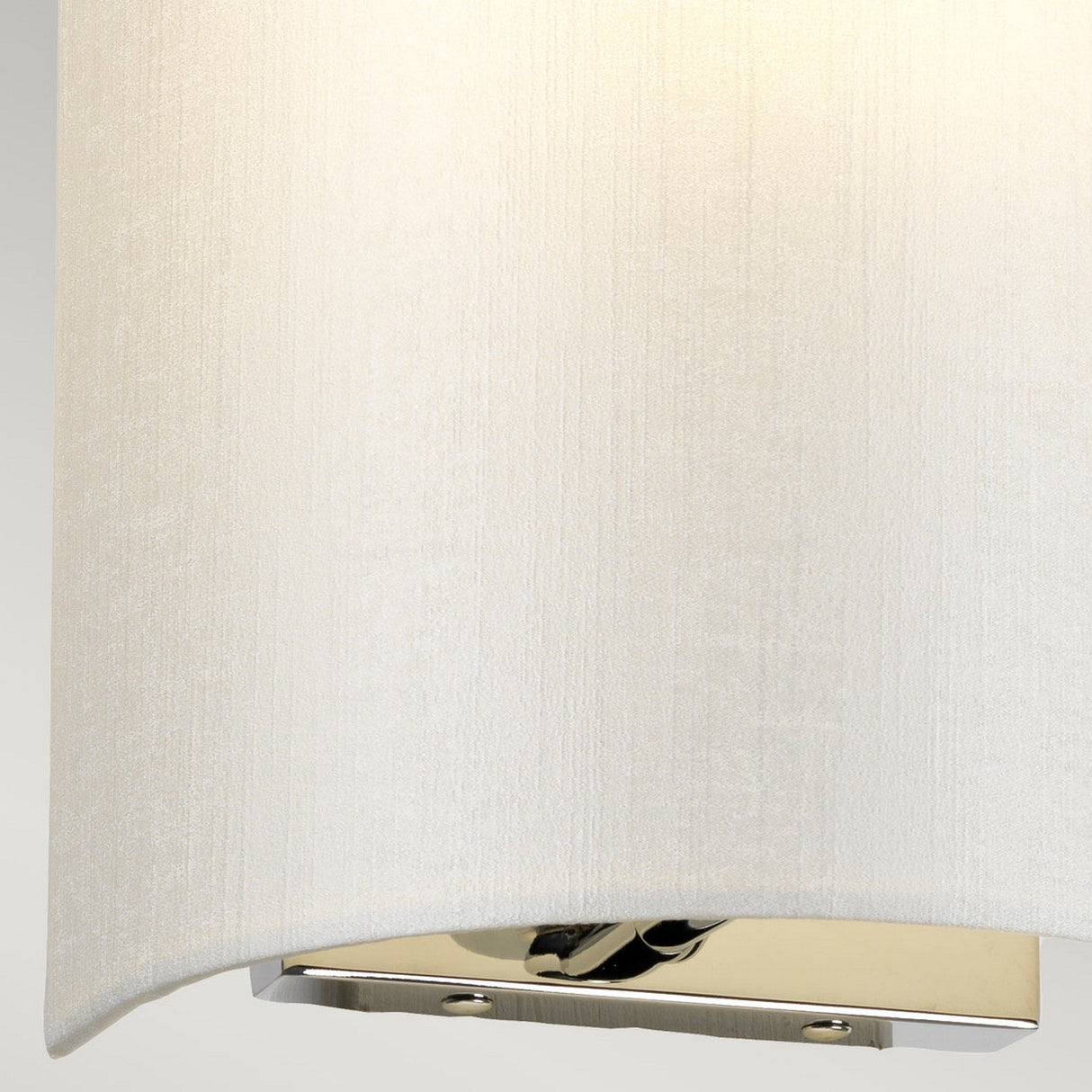 Close-up of the Cooper Small Curved Wall Light, highlighting its compact design with a simple, cylindrical white fabric shade and polished chrome base. This modern wall fixture emits a soft, warm glow that enhances the texture of the fabric.
