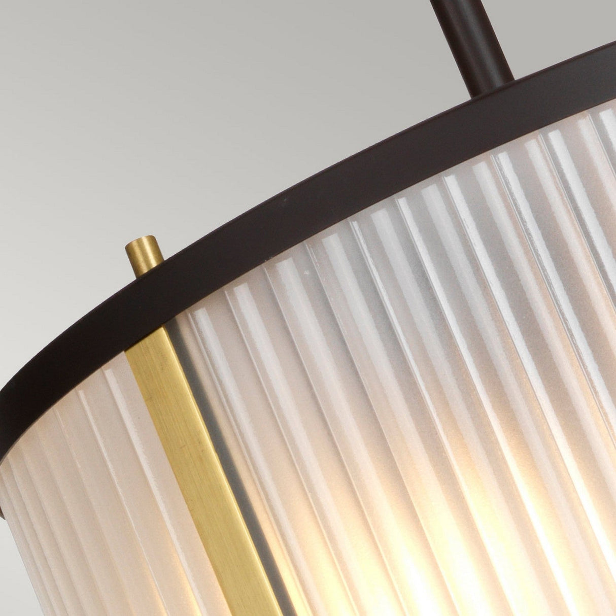 Close-up of the Corona 2 Light Pendant / Semi-Flush in Bronze Dark Brown, showcasing its cylindrical frosted glass shade. The pendant lamp is adorned with vertical ridges, a brass strip accent, and a black top edge, casting a warm glow against a neutral background that highlights its subtle bronze dark brown finish.