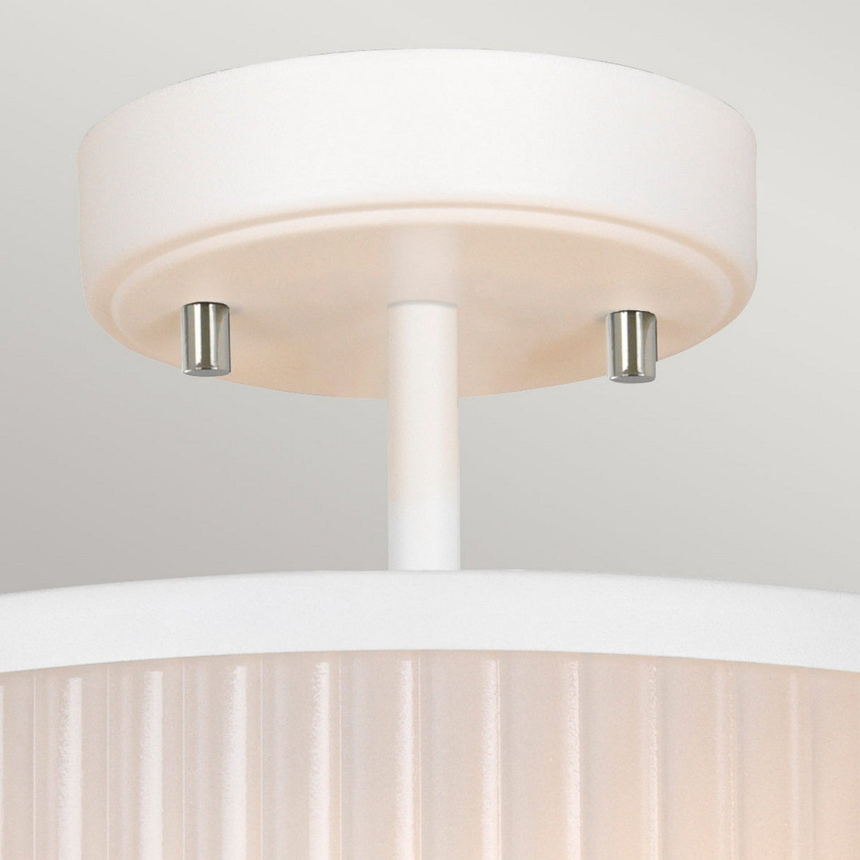 A close-up view of the Corona 2 Light Pendant / Semi-Flush in White Satin showcases its modern design, characterized by a cylindrical base accented with two small bolts. The ribbed, textured shade adds a touch of sophistication as it is mounted against a plain, light-colored ceiling, offering an elegant and contemporary look.