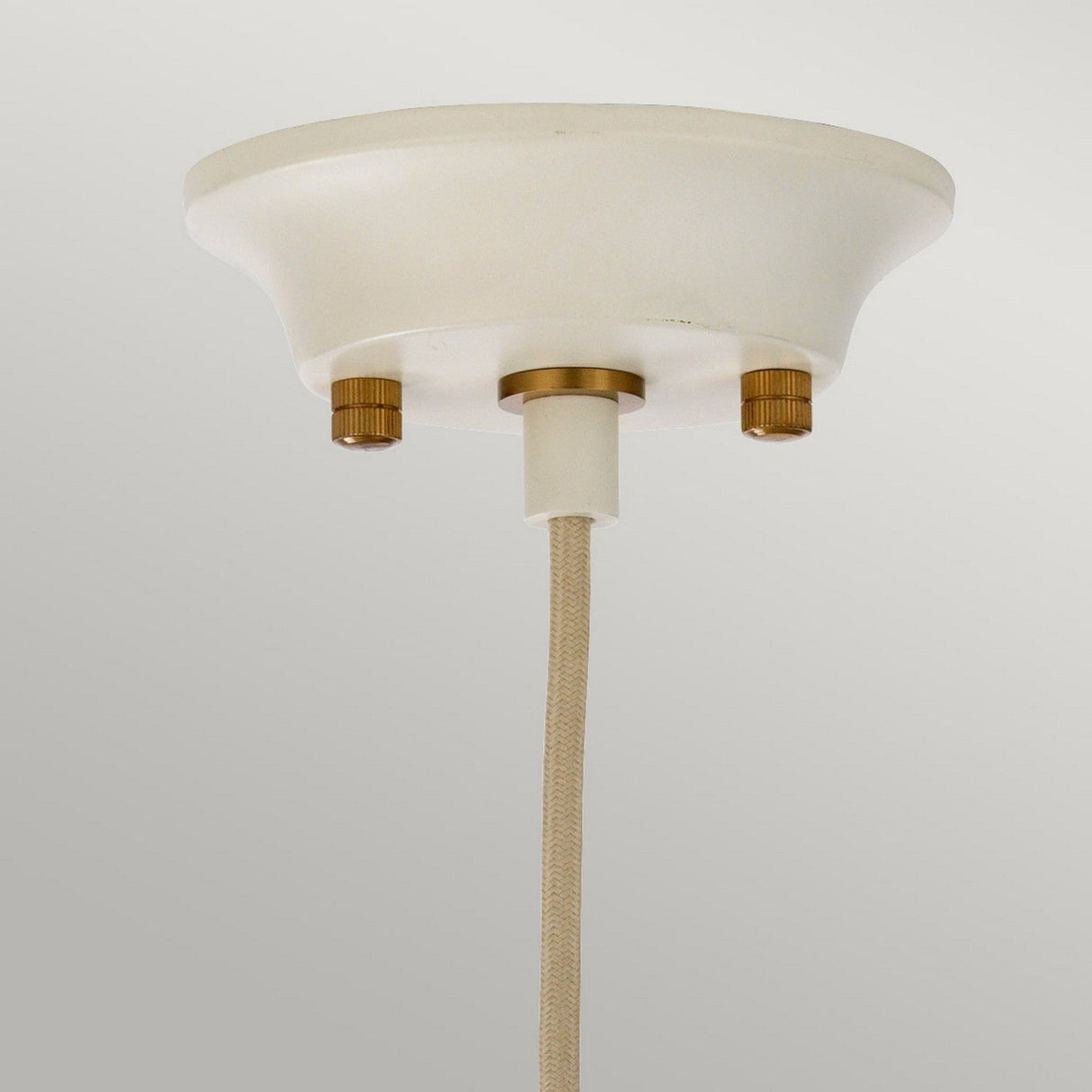 The Cosmos 1 Light Pendant in cream, elegantly showcases its retro style as it hangs from the ceiling. The conical base, painted in creamy tones and accented with aged brass details including two round brass knobs, is complemented by a fabric-covered cord. Its sleek design pairs beautifully against the light gray background.