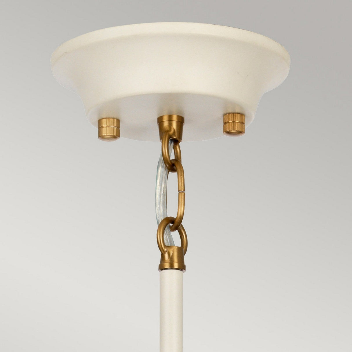 Close-up of the Cosmos 5 Light Pendant showcasing its cream-painted canopy and retro-inspired design elements. The aged brass chain link and fittings connect to a white rod and hand-blown glass shades, set against a plain, light gray background.
