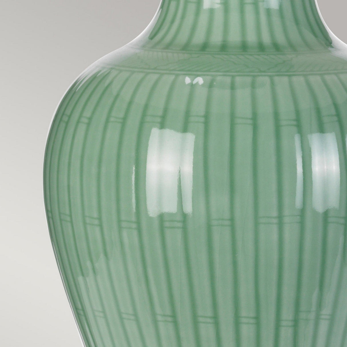 Close-up of a Dalian Table Lamp with Celadon finish, showcasing its vertical ribbed, green patterned ceramic base with a glossy surface. The lamp's texture and elegant design are highlighted by reflections of light, reminiscent of an Oriental vase.