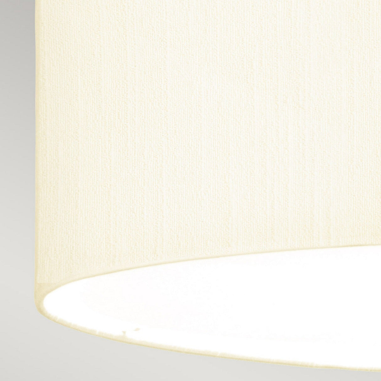 A close-up view of the Fletcher 22" Flush features its cylindrical faux silk ivory shade. The texture of the fabric is visible as the light within gently illuminates the interior, casting a soft glow. Paired with an aged brass fixture, it stands gracefully against a neutral gray backdrop.