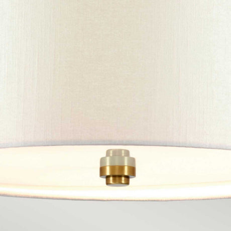 A close-up of the Fletcher 30" Flush - Aged Brass With Ivory Shade showcases the aged brass detail beneath its faux silk ivory shade. The lamp is illuminated, emitting a soft glow, and the neutral light gray background highlights its modern elegance.
