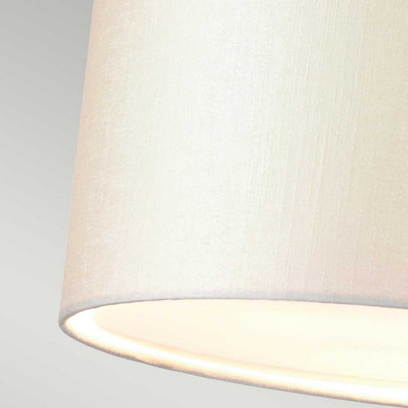 Close-up of an ivory fabric lampshade emitting a soft, warm light set against a light gray background, reminiscent of the elegant Fletcher 34" Flush - Aged Brass with Ivory Shade. The texture of the fabric appears smooth and slightly woven, complementing the aged brass ceiling fixture beautifully.