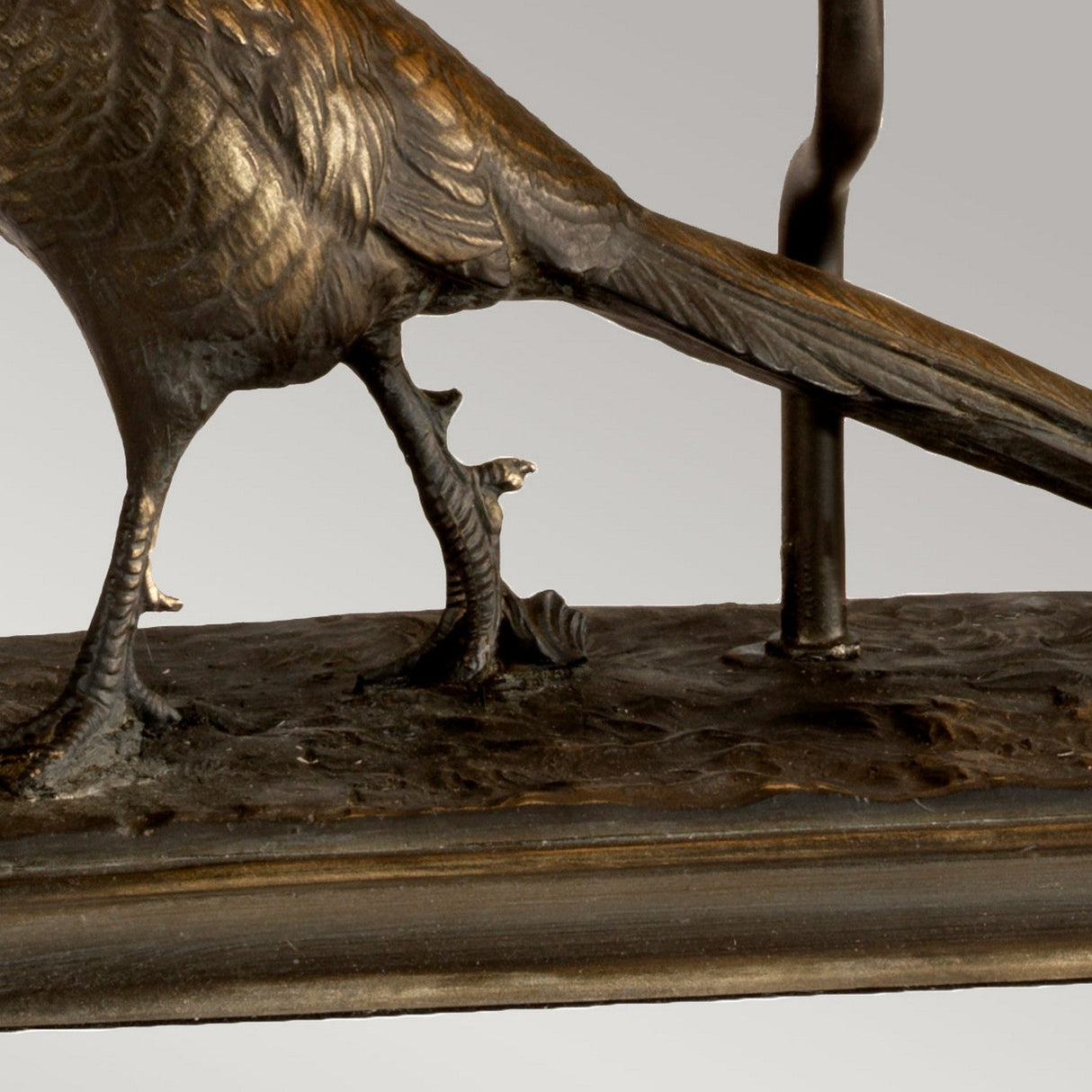 A close-up view of the lower body and legs of the Halkirk Table Lamp With Rectangle Shade - Bronze Patina, featuring detailed feathers and talons on a textured base, with part of a support structure visible behind it.