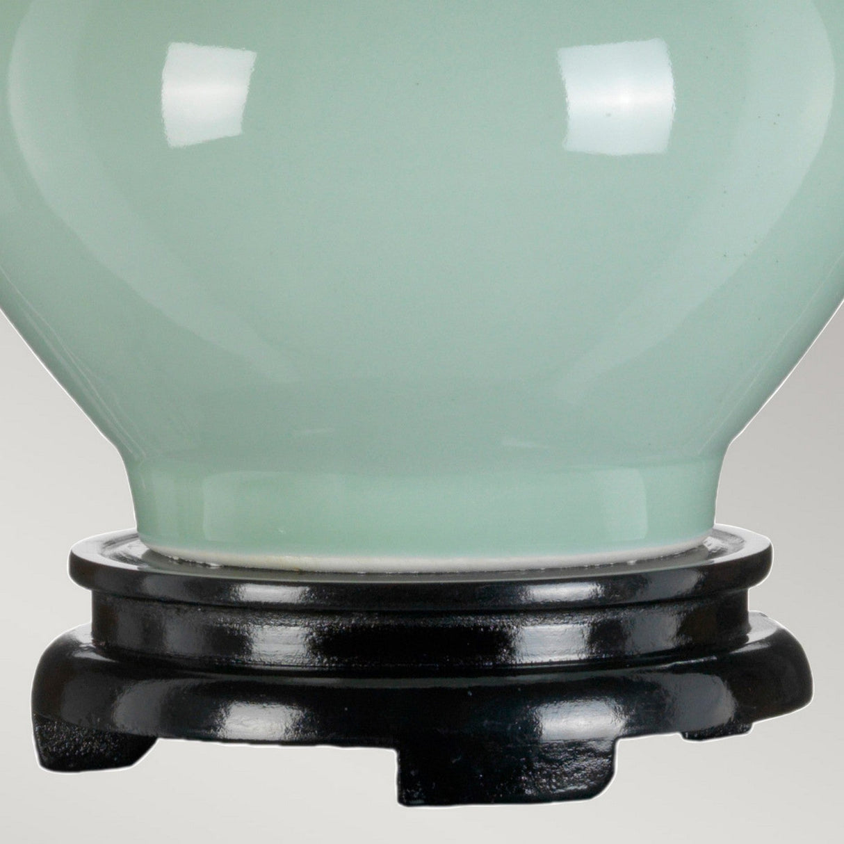 A close-up of the Harbin Gourd Table Lamp with a tall empire shade in celadon, featuring a glossy, pale green ceramic base that resembles a gourd. It sits on a round, black wooden base and its smooth, curved surface with subtle reflections underscores its shiny elegance.