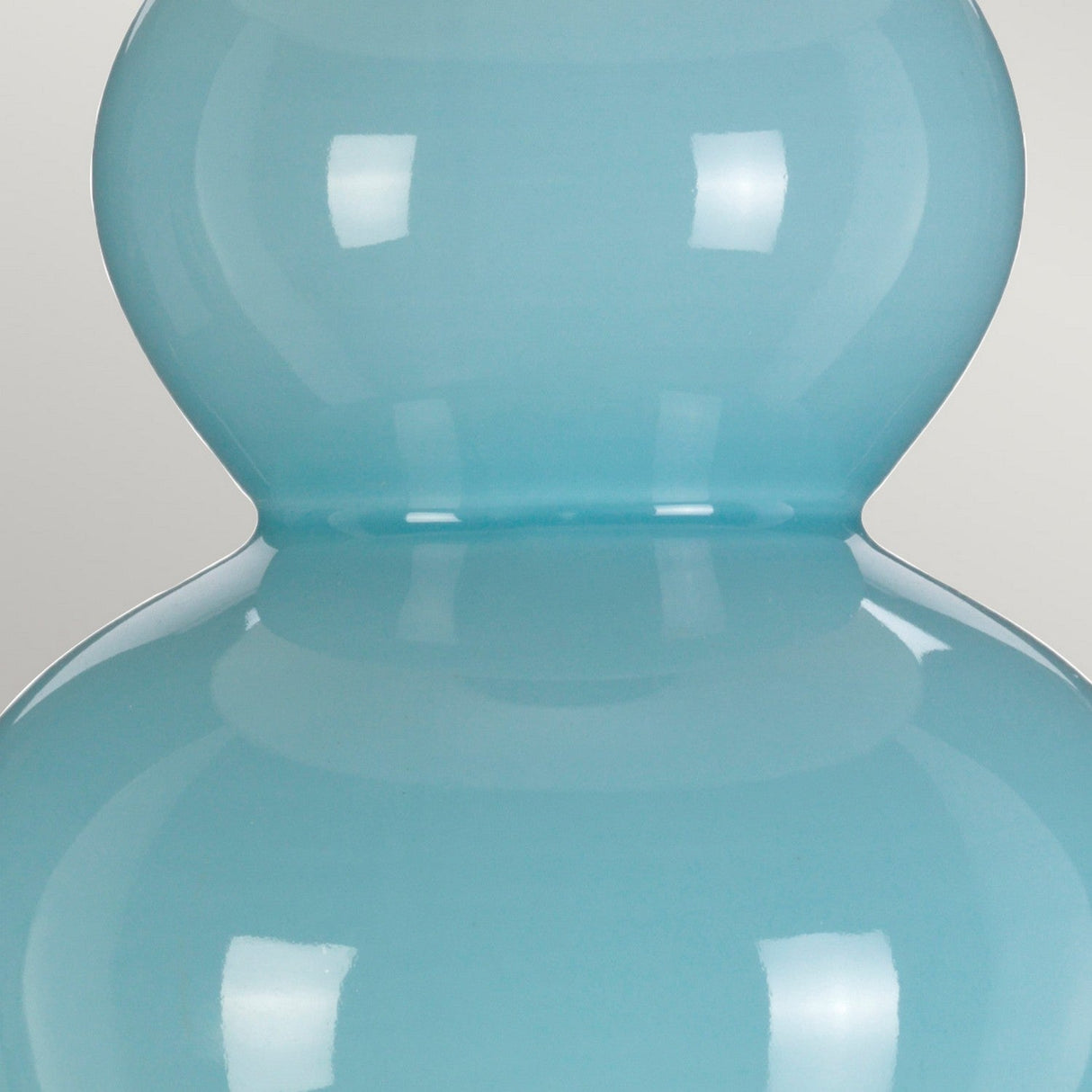A close-up of the Harbin Gourd Table Lamp with a tall empire shade in duck egg blue reveals its smooth, rounded shape. The high sheen finish reflects light beautifully, set against a plain, light gray background.