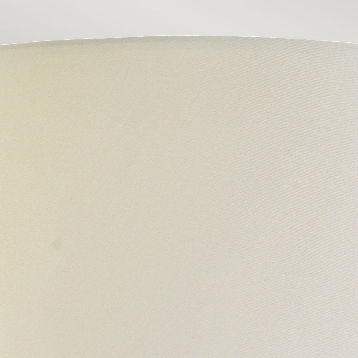 A close-up of a smooth, off-white surface showcases subtle texture, with a gentle curve at the left edge. The lighting casts a delicate shadow on the base of the Harbin Gourd Table Lamp With Tall Empire Shade in Oxblood, accentuating its minimalist and serene design.