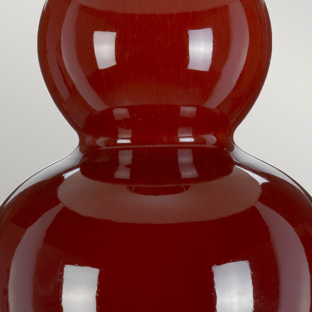 Close-up of a glossy, deep red, gourd-shaped ceramic vase with a reflective surface. The image highlights the sleek curves and smooth texture reminiscent of the Harbin Gourd Table Lamp With Tall Empire Shade - Oxblood, showcasing its stunning shiny finish.