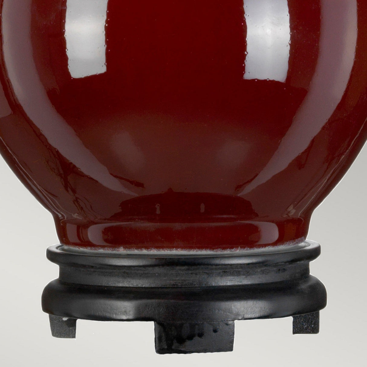 The image captures a Harbin Gourd Table Lamp in an oxblood finish, featuring a glossy ceramic body. The bottom of the lamp shows a hint of its black wooden base against a softly elegant gray background, evocative of the sophistication found in an Empire shade.