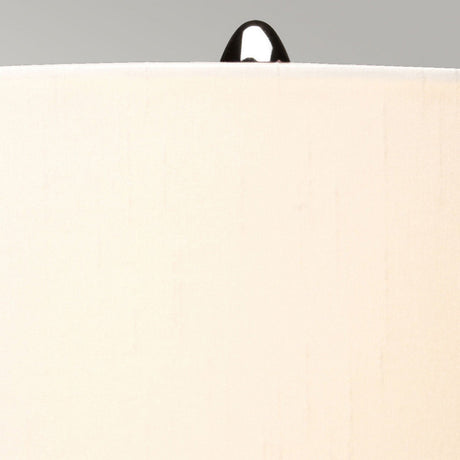 Close-up of a beige lampshade featuring a polished nickel finial atop, set against a neutral gray background. The smooth texture of the lampshade and the reflective quality of the finial beautifully accentuate the elegant style of the Kara Table Lamp - Polished Nickel - Blue Glass.