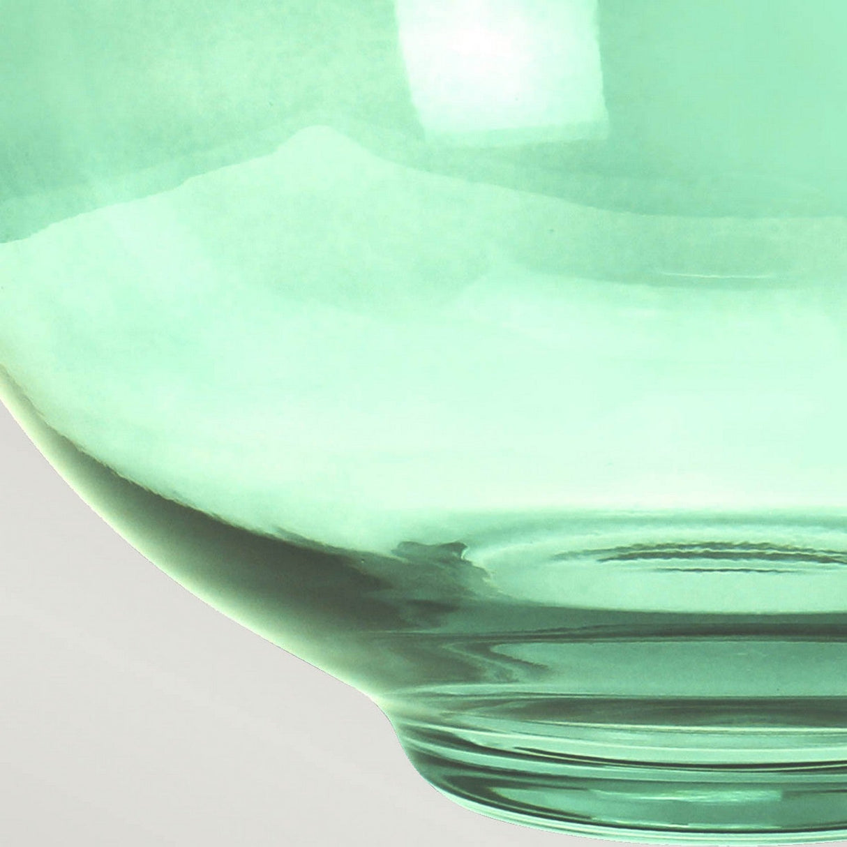 The close-up of the Kara Table Lamp in aged brass with its translucent, dark green glass bowl reveals a smooth, curved surface. Light softly reflects off the glass, highlighting its elegant contours against a neutral background. This piece beautifully embodies both elegance and timeless charm.