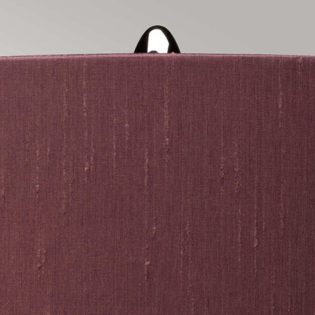 A close-up of a textured, reddish-brown fabric against a gray background reveals a black loop or tag at the top center, suggesting it might be part of the back of a chair or similar object. Envision this sophisticated scene enhanced by the polished nickel and smoke glass base of the Kara Table Lamp - Polished Nickel - Smoke Glass.