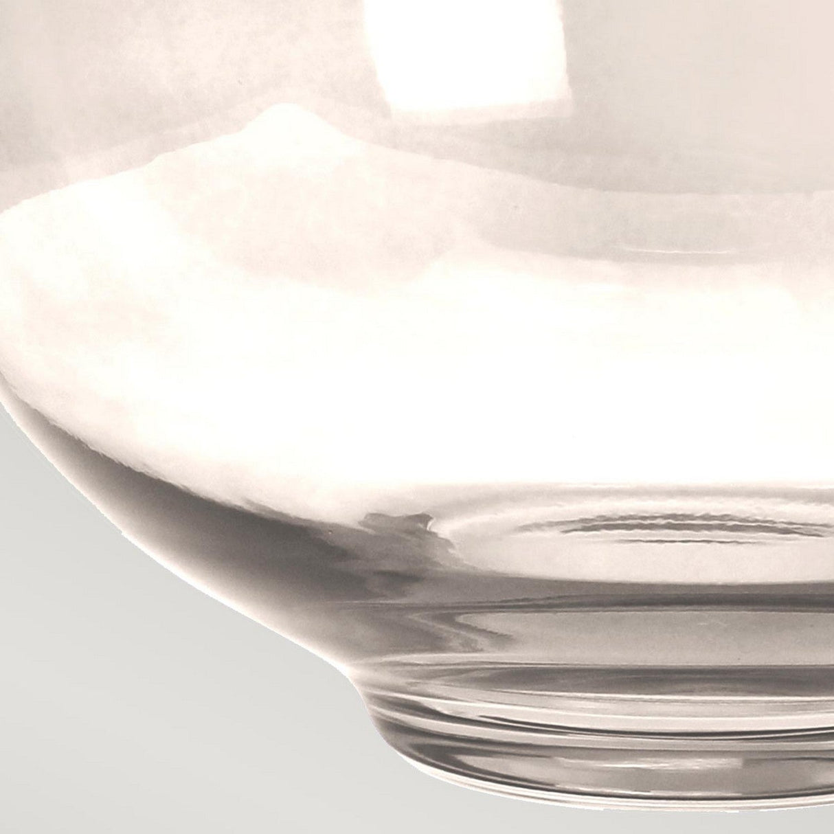 Close-up of a clear, transparent glass bowl against a light gray background. The bowl's rim and curved shape are visible, highlighting its smooth and shiny surface, reminiscent of the elegant design found in the Kara Table Lamp - Polished Nickel - Smoke Glass collection.