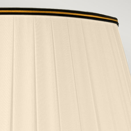 Close-up of a luxurious tall Empire shade in beige adorned with vertical pleats and accented by a black trim featuring a delicate yellow stripe at the top. The image beautifully showcases the fabric's texture and detail under soft lighting, perfectly complementing the Louviers Table Lamp in Oxblood & Gold.