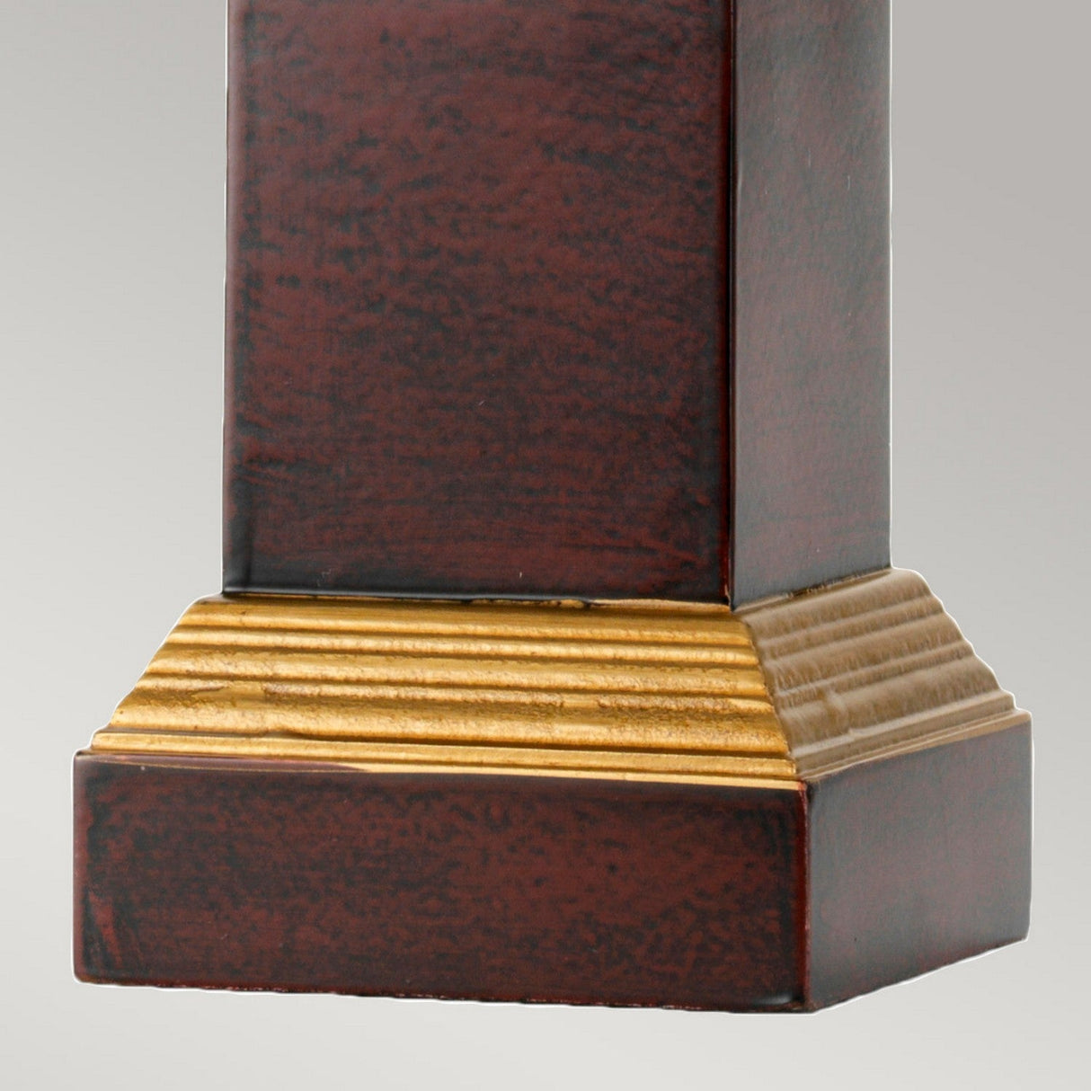 Close-up of the Louviers Table Lamp, showcasing its wooden column with a brown finish and a golden, ridged base that enhances its luxurious aesthetic. The Oxblood & Gold Tall Empire Shade complements the elegant design against a neutral gray background.