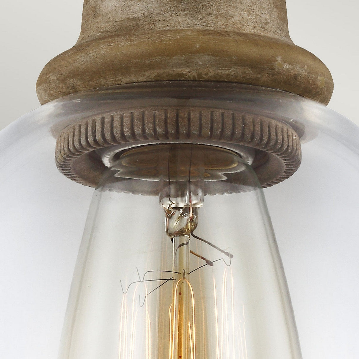Close-up of an Edison-style light bulb with a visible filament, encased in a clear glass cover, and mounted in the Matrimonio 1 Light Mini Pendant fixture, featuring textured driftwood and dark weathered zinc for a charming rustic lighting effect.