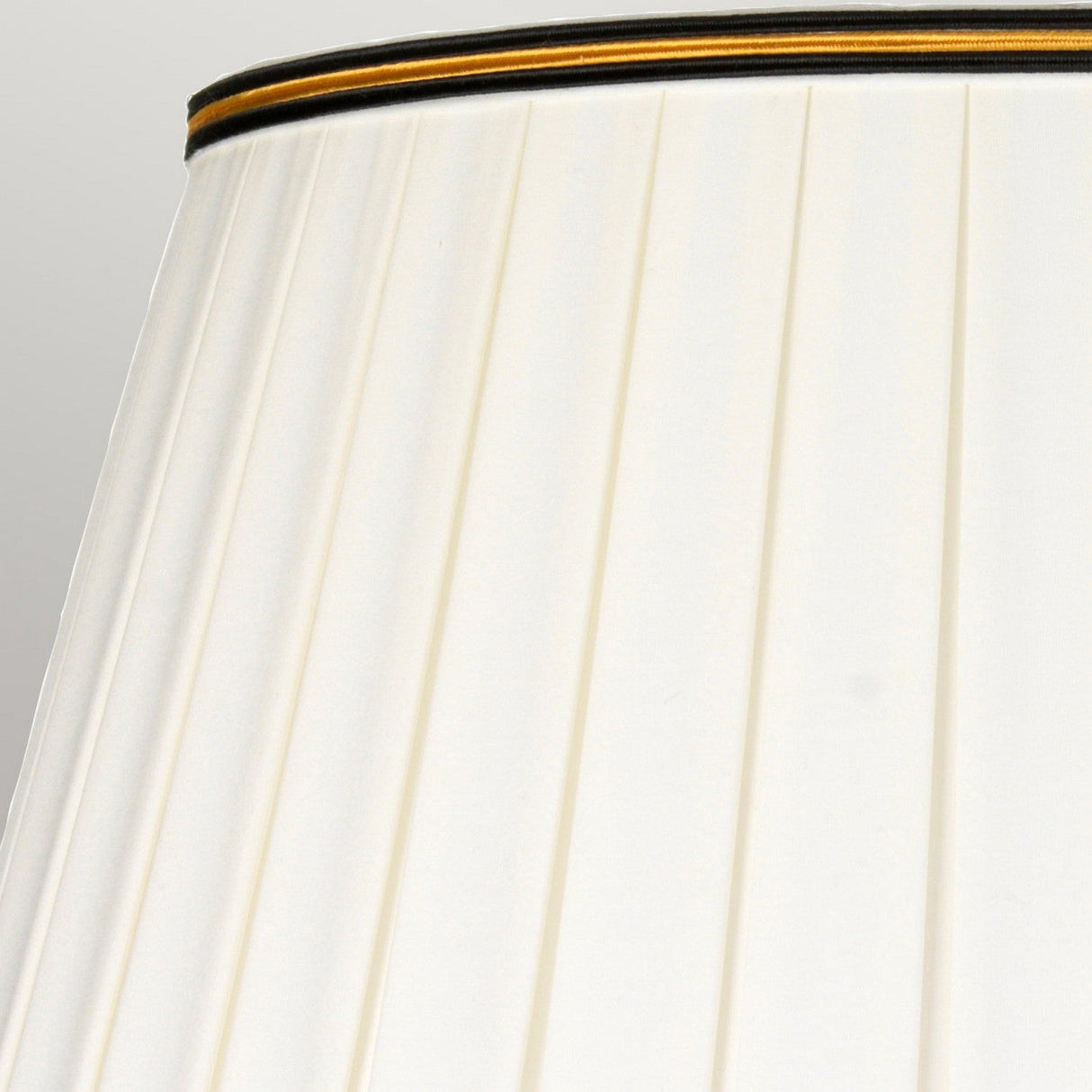 Close-up of the elegant Narbonne Table Lamp - Black & Gold's pleated cream-colored shade with dark trim. Set against a light gray background, the pleats create a striking pattern of vertical lines, embodying sophisticated design.
