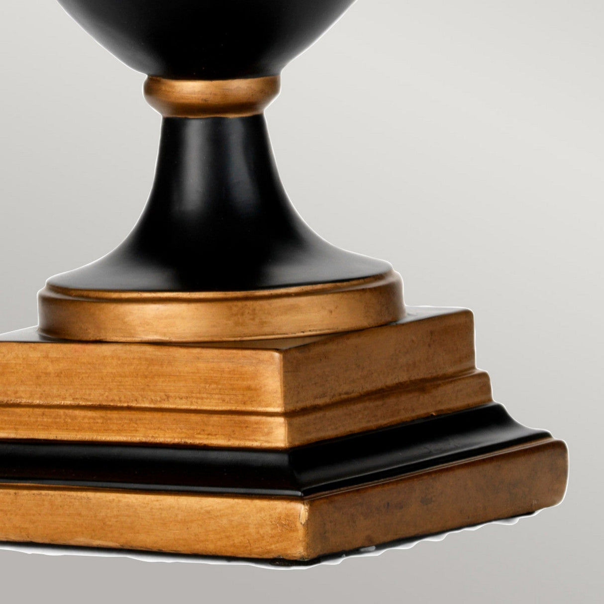 Close-up of the base of the Narbonne Table Lamp - Black & Gold, showcasing its elegant black and gold color scheme. The base exhibits a stacked, square design with a glossy black finish complemented by gold trim, delivering a formal and sophisticated look.