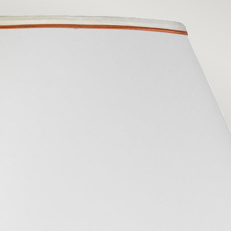 Close-up of a white lampshade featuring beige trim set against a light gray backdrop. The smooth, subtly angled surface captures gentle lighting, exuding an oriental elegance reminiscent of the Oxblood Temple Jar Table Lamp with Tall Empire Shade in Oxblood.