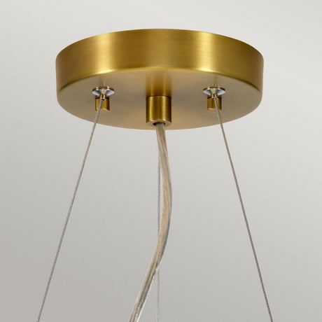 A close-up of the Pearce 14" Pendant Light in aged brass and ivory shade highlights two cables connected to a round base. The fixture hangs elegantly from the ceiling with a single power cord at its center, set against a simple, light grey background.