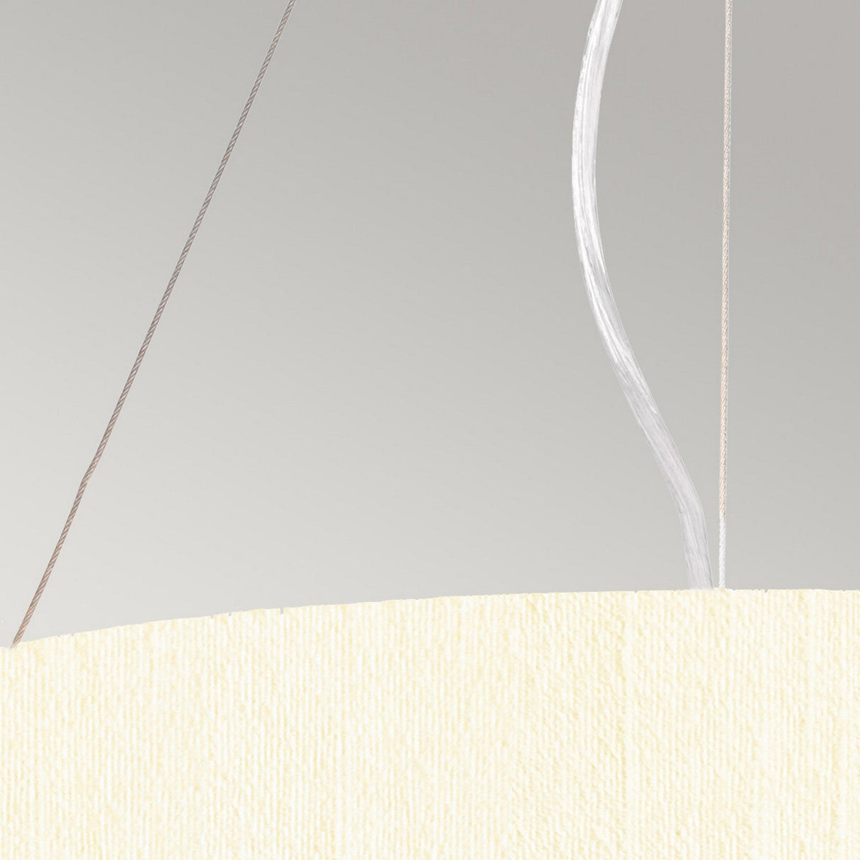 A close-up of the Pearce 18" Pendant Light, featuring a textured ivory shade set against a light gray backdrop, highlights its modern design. Two wires, one white and one brown, rise from the top of this elegant pendant fixture in polished chrome.