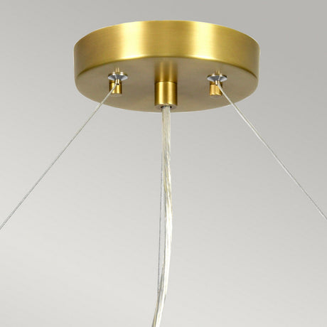 The Pearce 26" Pendant Light features an aged brass metallic base and an ivory shade. It is suspended from the ceiling by three wires, set against a neutral gray background that accentuates its sleek and minimalist design.